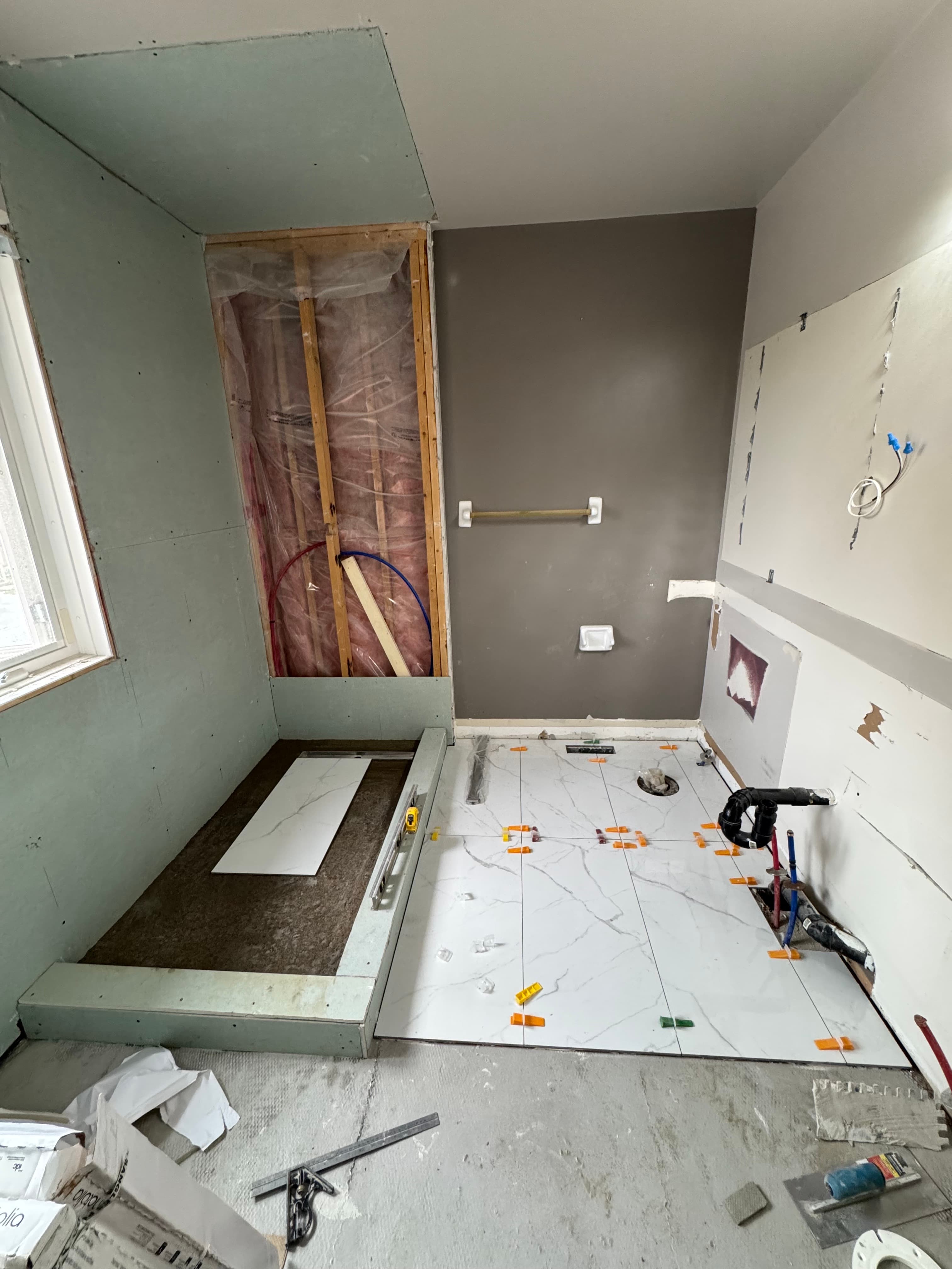 Marble-look floor tiles being installed beside a shower base with leveling clips in place