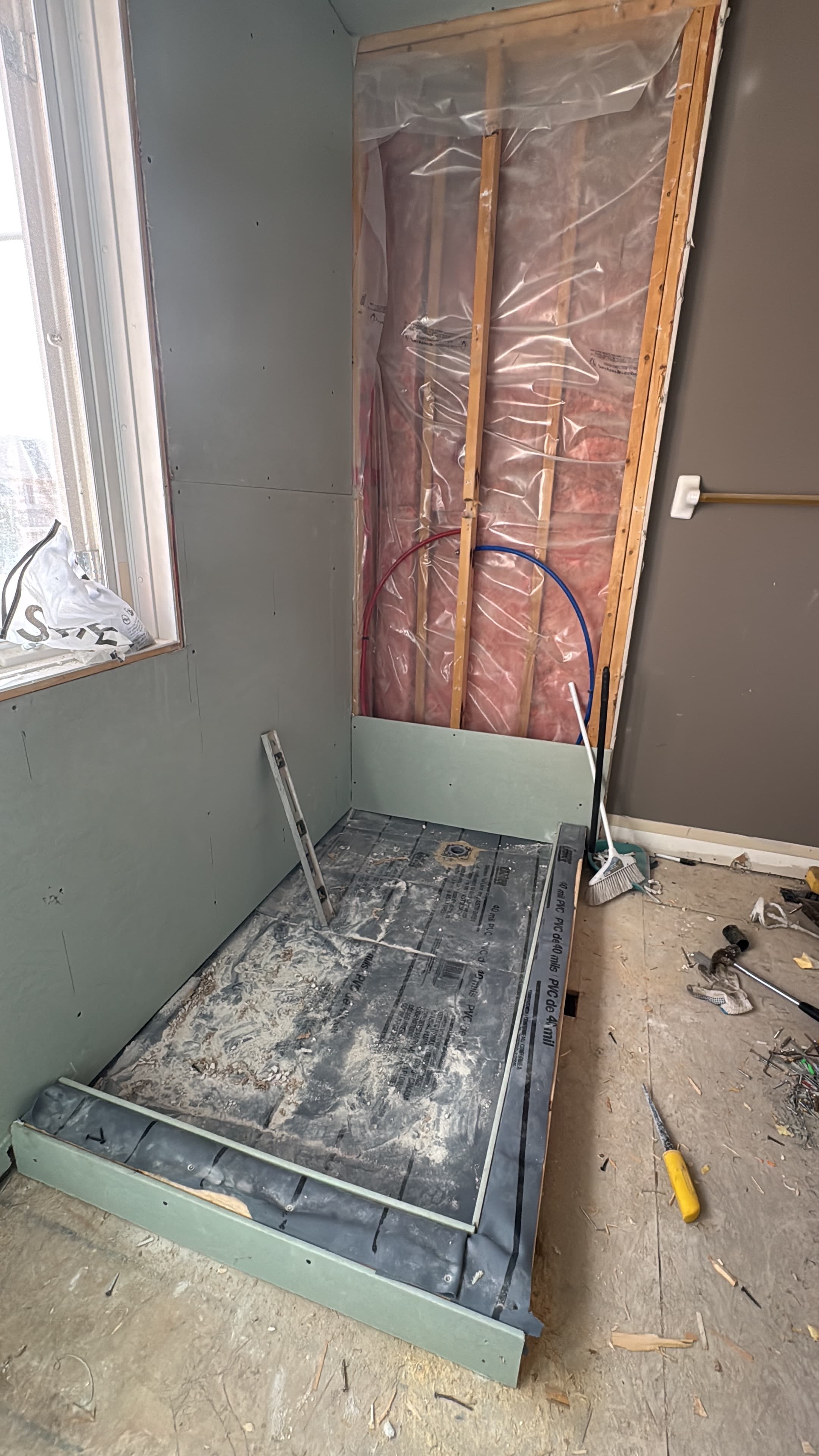 Shower area under construction with wall board, exposed plumbing, and a prepared shower base