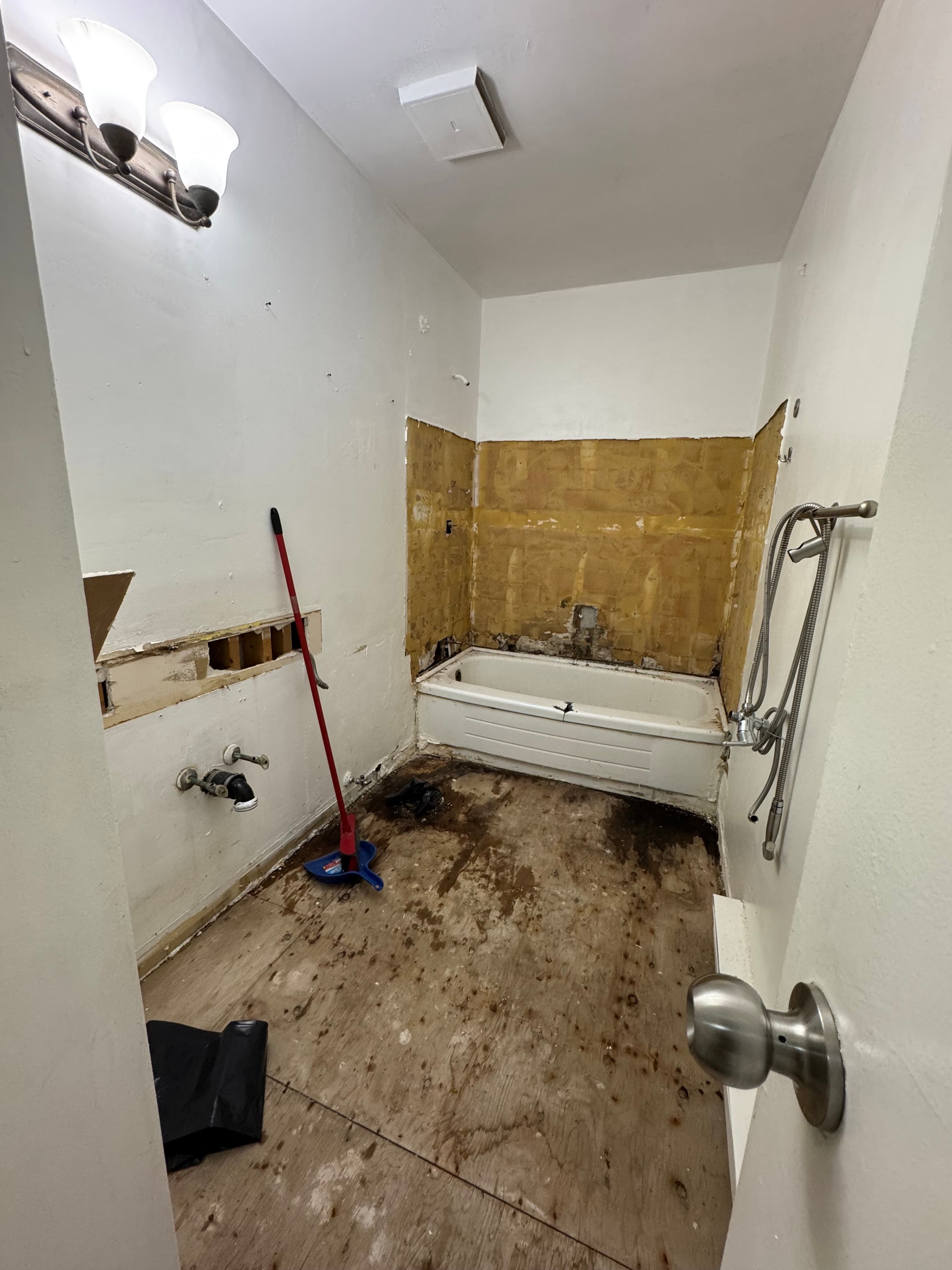Bathroom stripped back for renovation with the old bathtub, exposed subfloor, and removed wall finishes