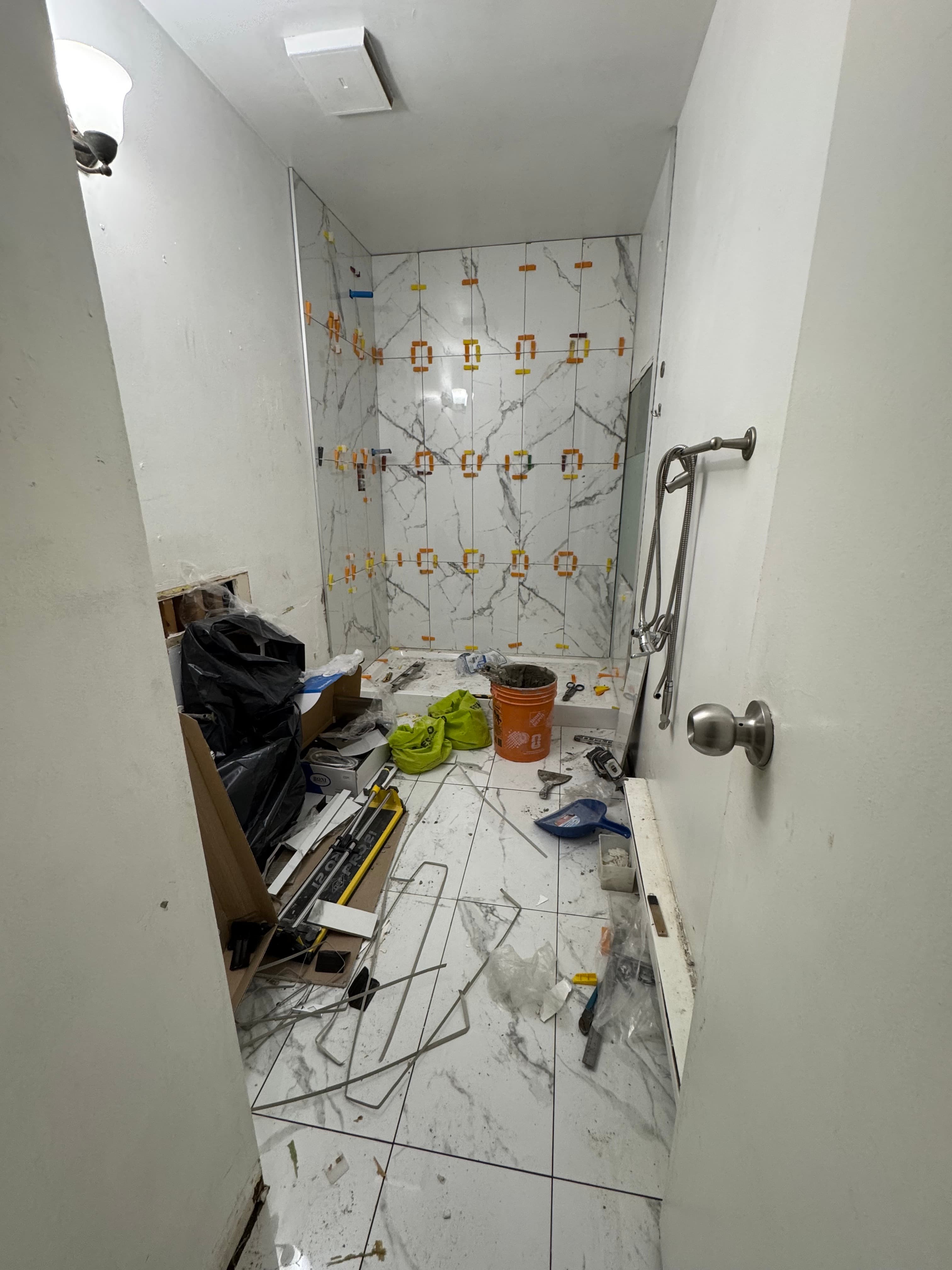 Marble-look shower walls being tiled with leveling clips and installation tools