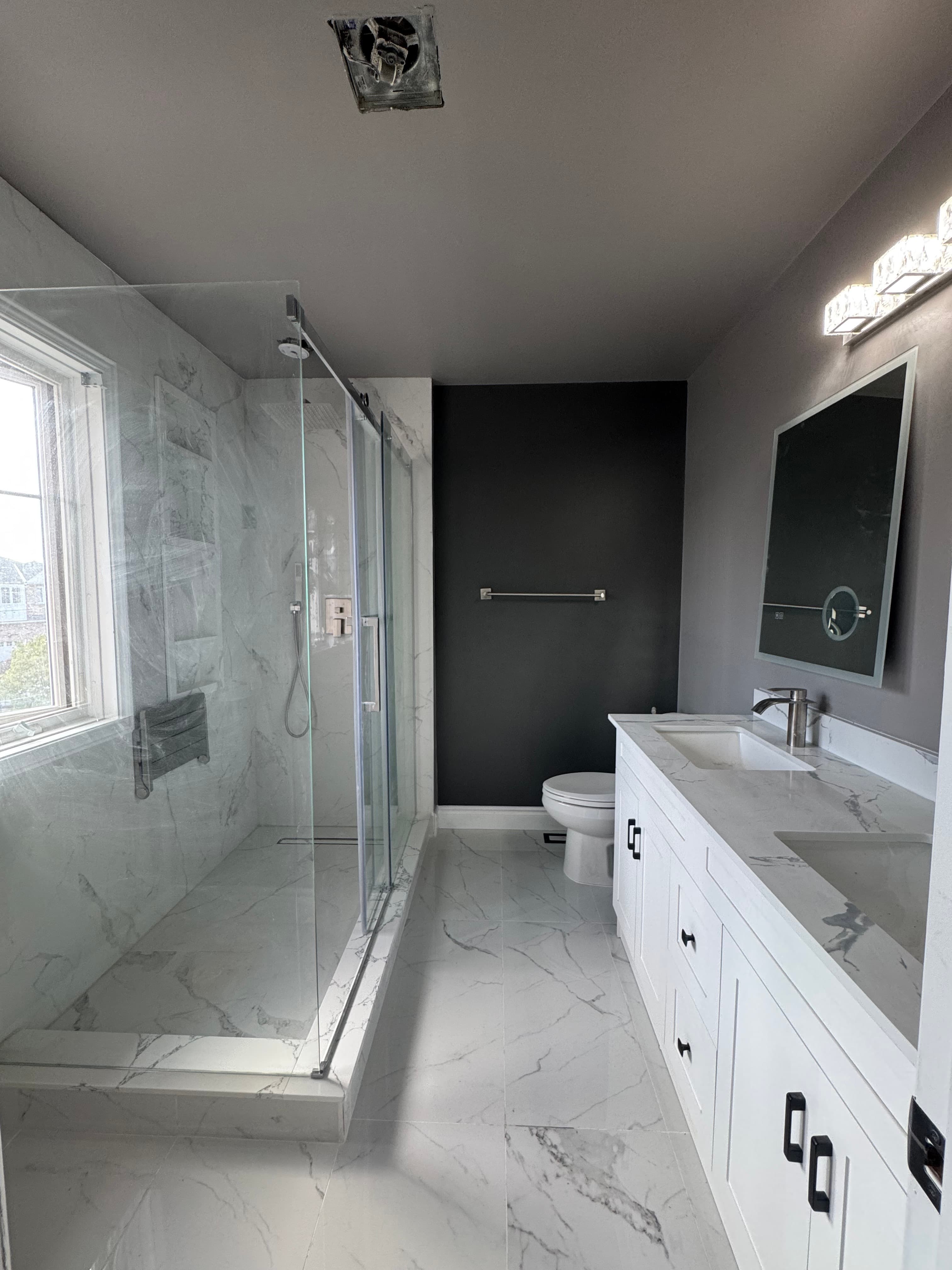Bathroom nearing completion with a glass shower, double vanity, marble-look floor, and dark accent wall