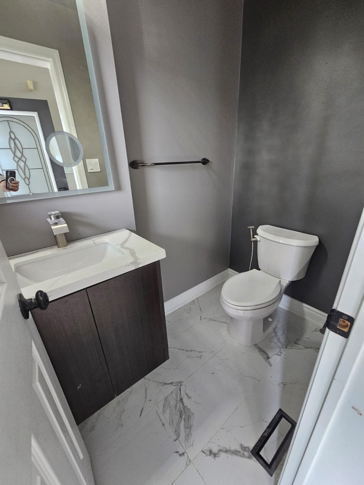 Powder room with dark vanity, marble-look countertop and flooring, and gray painted walls