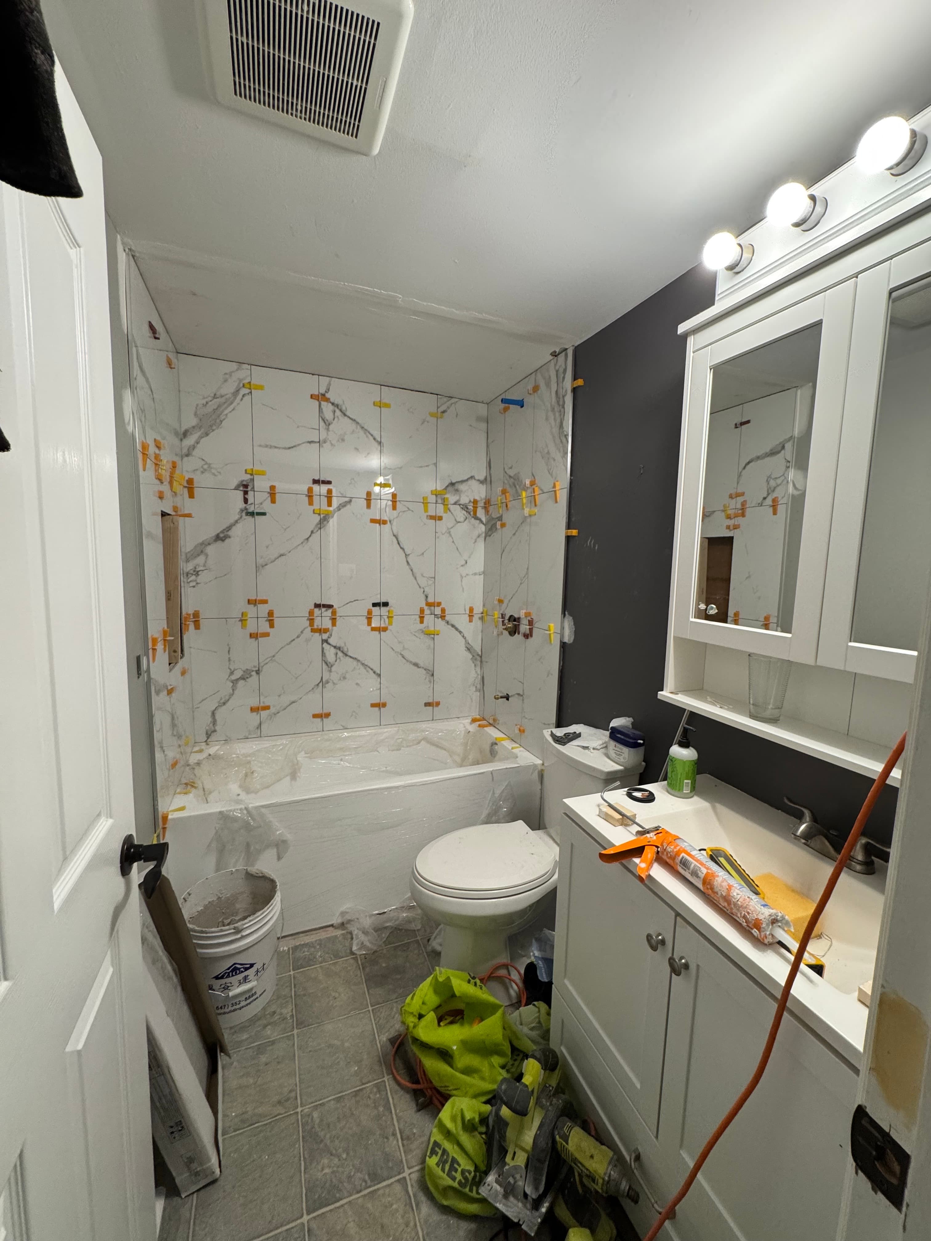 Marble-look tiles being fitted around a bathtub with leveling clips and protective covering