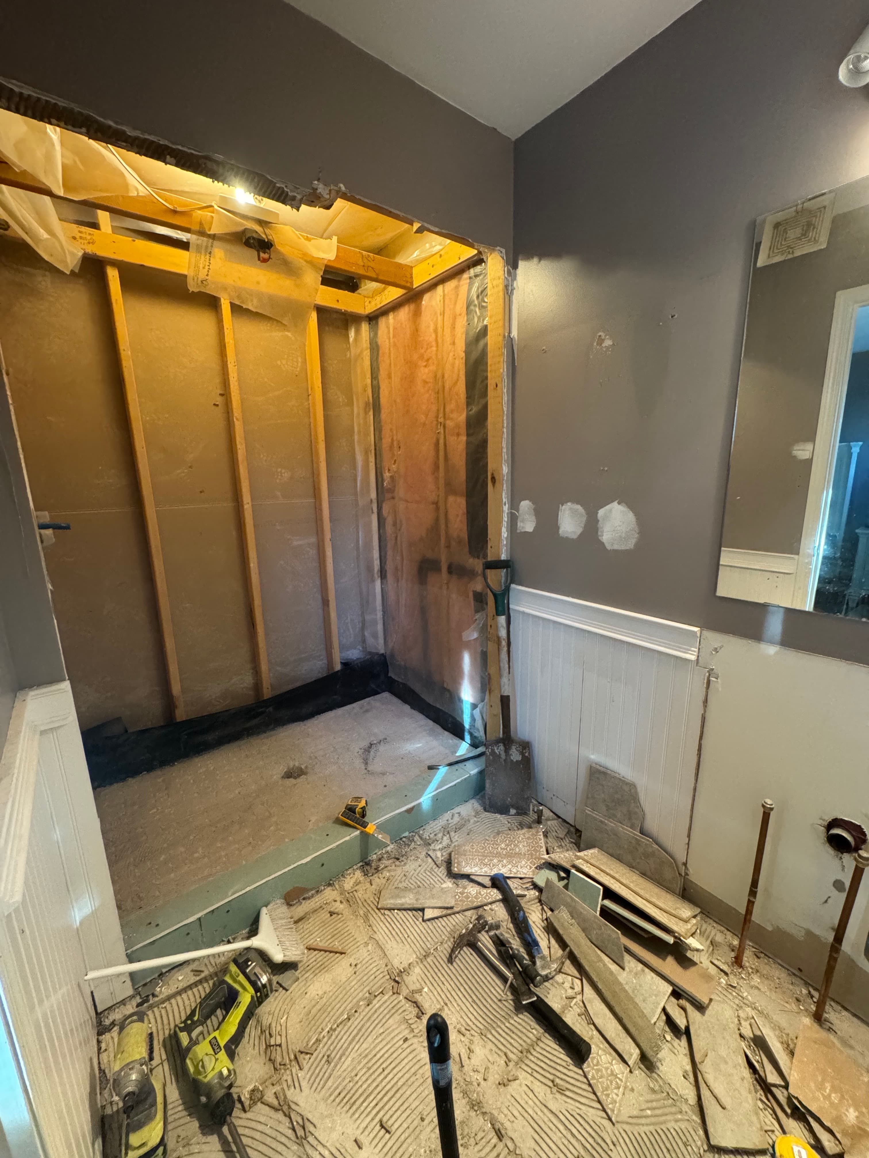 Shower demolition exposing framing and insulation with floor tile removal underway