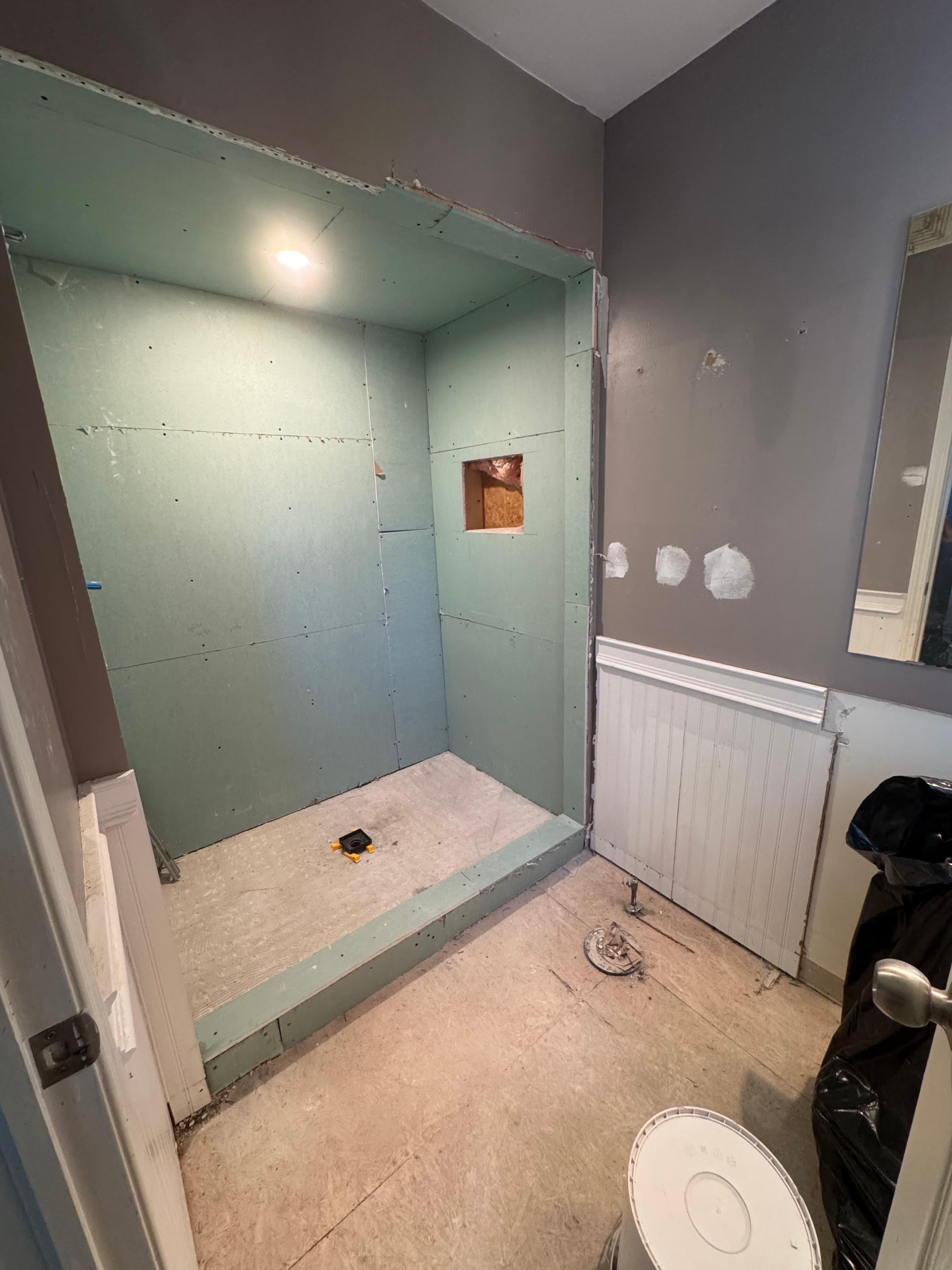 Walk-in shower under construction with wall board, a recessed niche opening, and a prepared shower floor