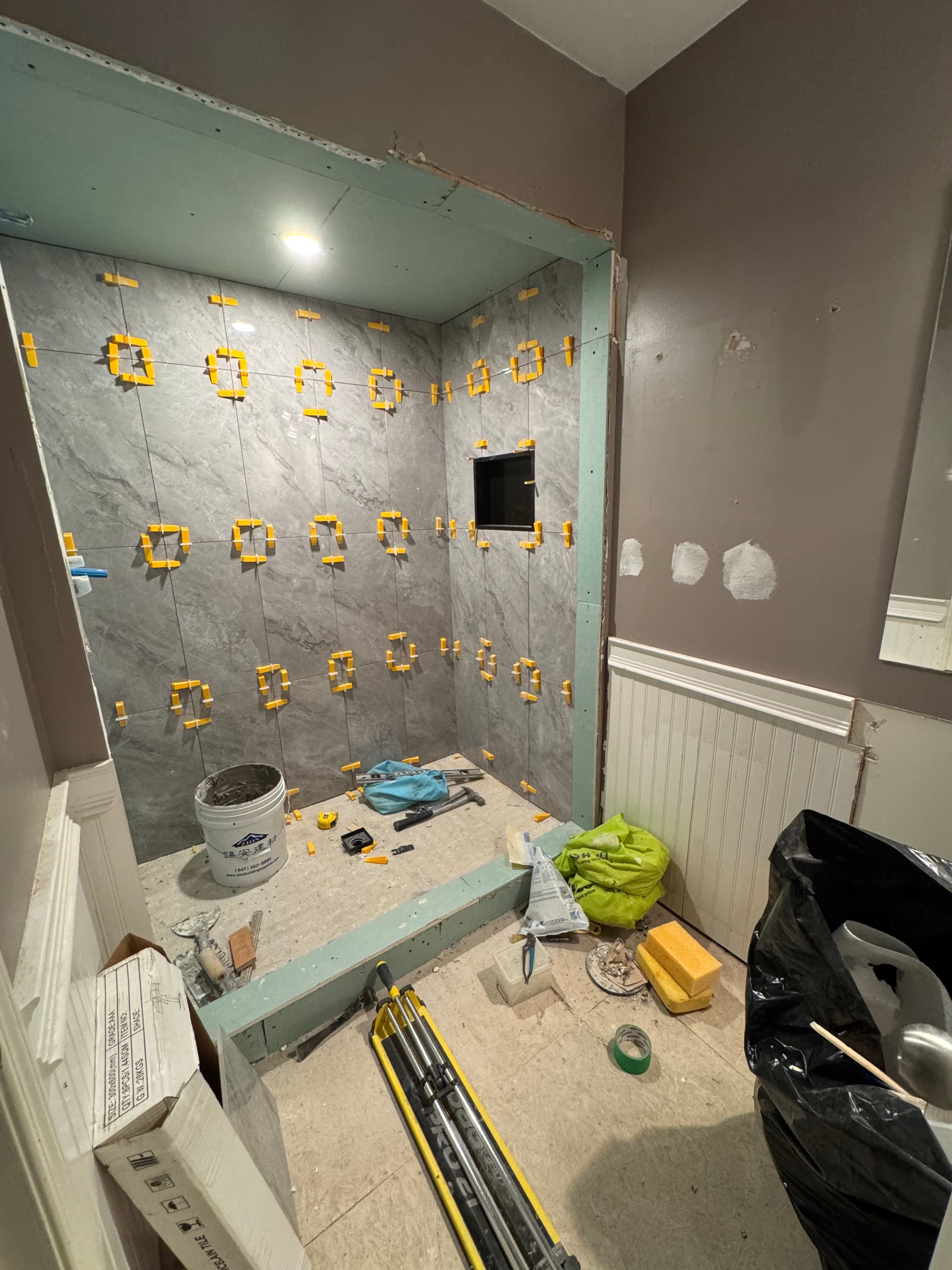 Large-format gray shower tiles being installed around a recessed niche with leveling clips
