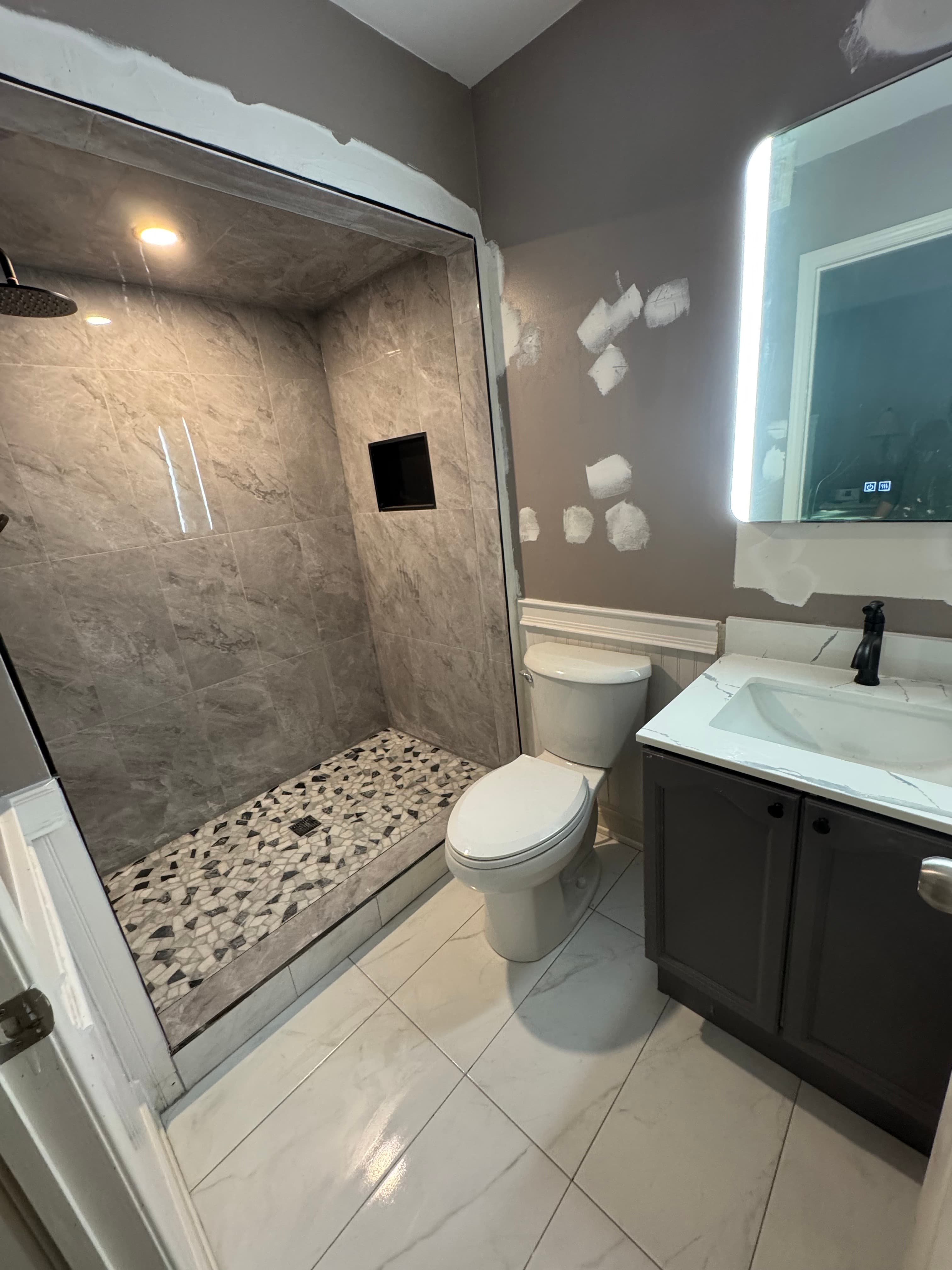 Bathroom during final wall preparation with a tiled walk-in shower, mosaic shower floor, dark vanity, and illuminated mirror